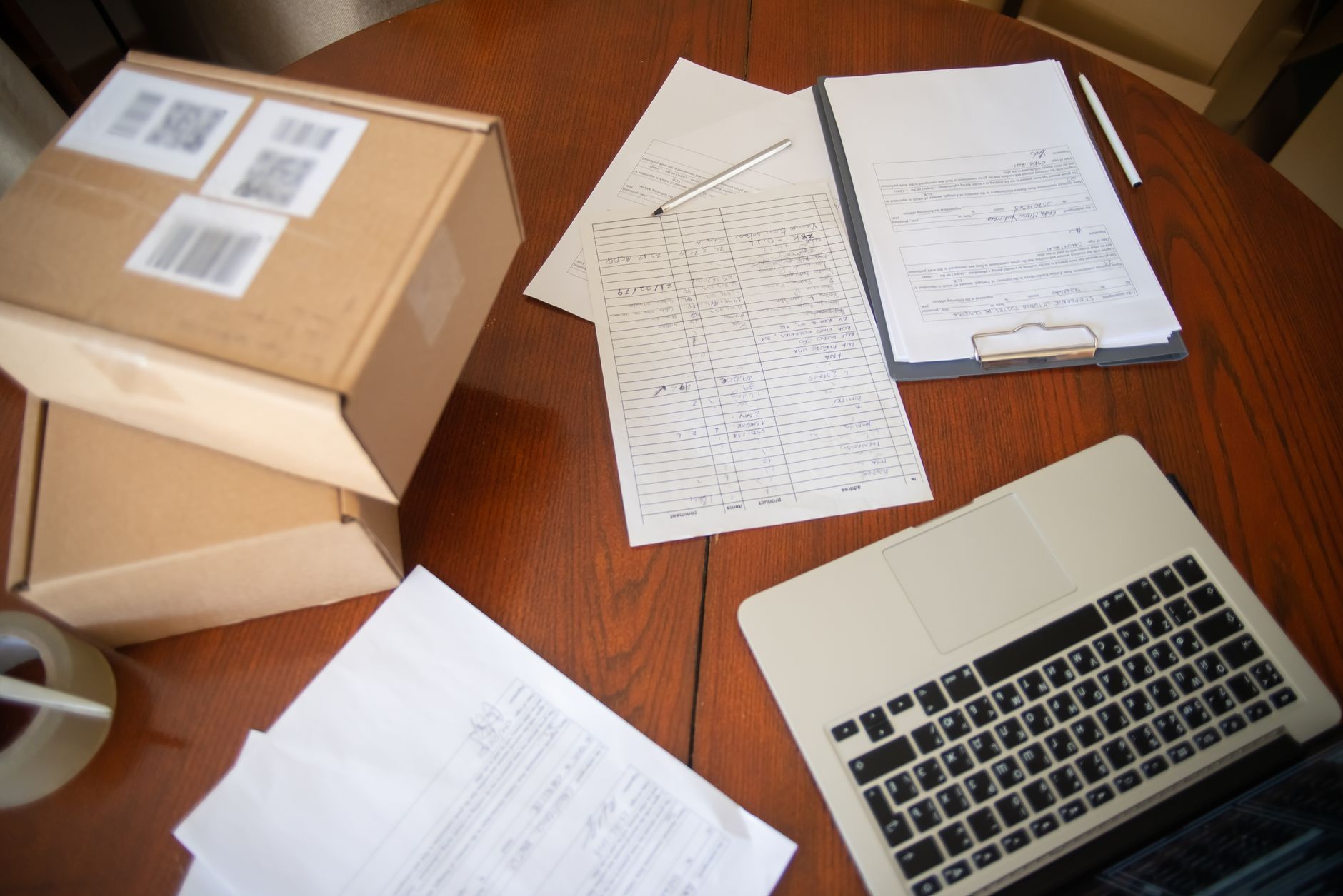 Vue en plan large d'un espace de travail avec ordinateur portable, documents et cartons pour une activité en ligne.